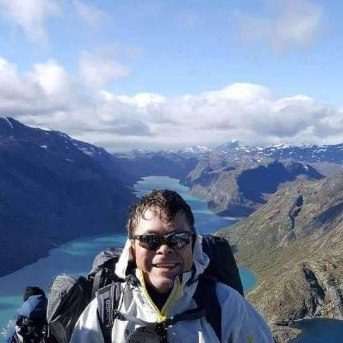 Knut Erik Jahr på tur i Jotunheimen, med fjell og en grønn innsjø bak seg